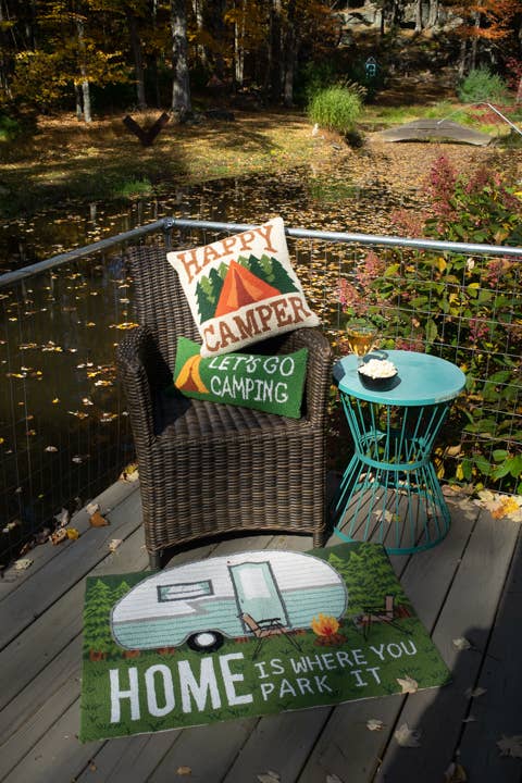 Chair with 'Happy Camper' pillow and 'Let's Go Camping' sign on a deck by a pond.