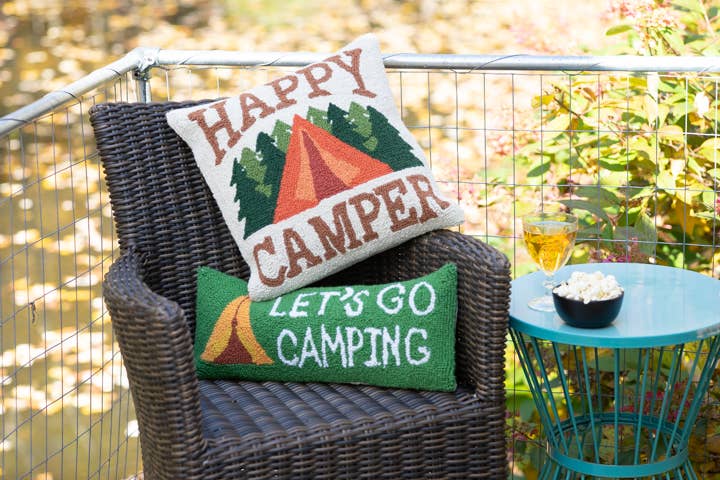 Decorative pillows with 'Happy Camper' and 'Let's Go Camping' text on a chair outdoors.