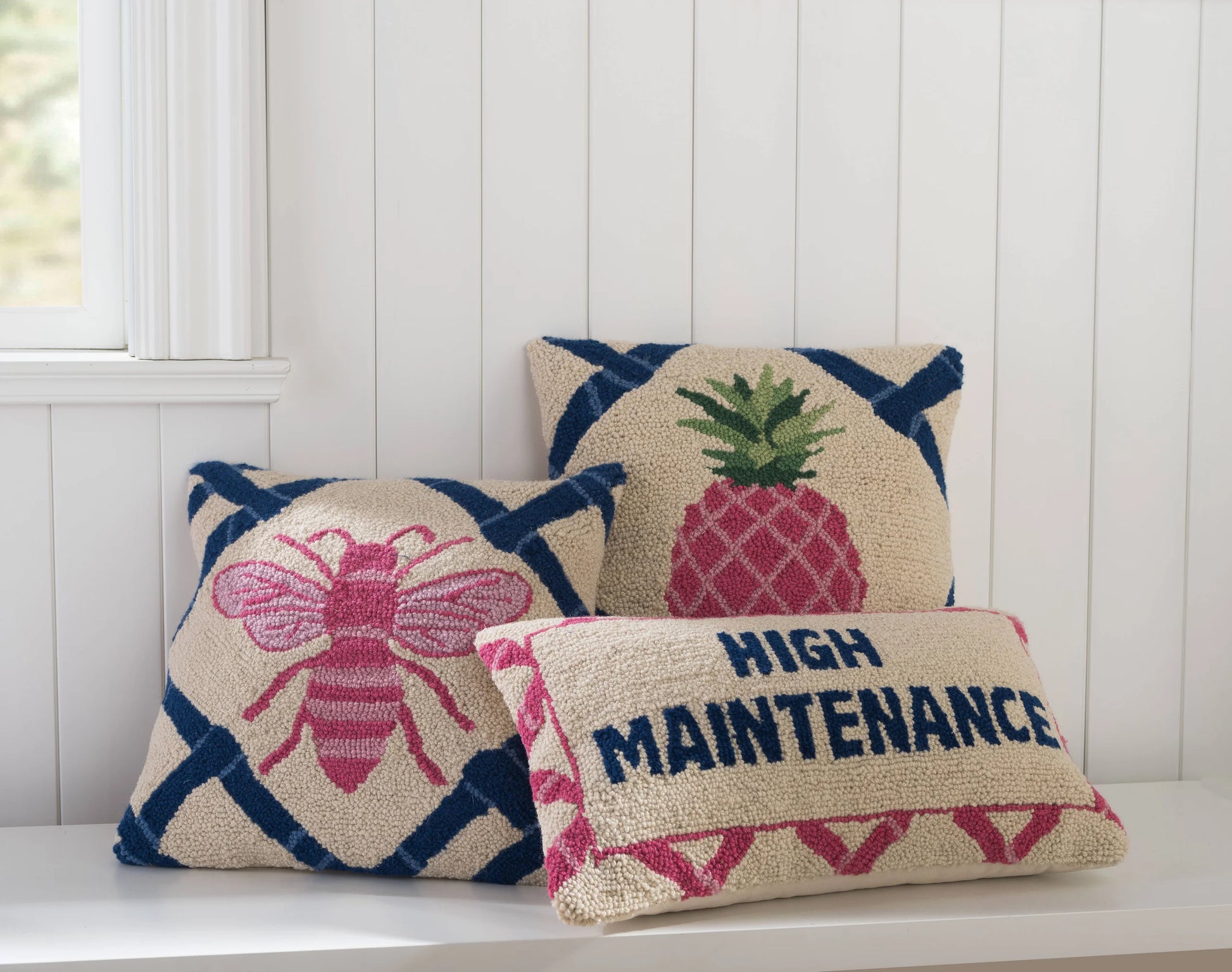 Three decorative pillows with pineapple, bee, and 'High Maintenance' designs on a white surface.