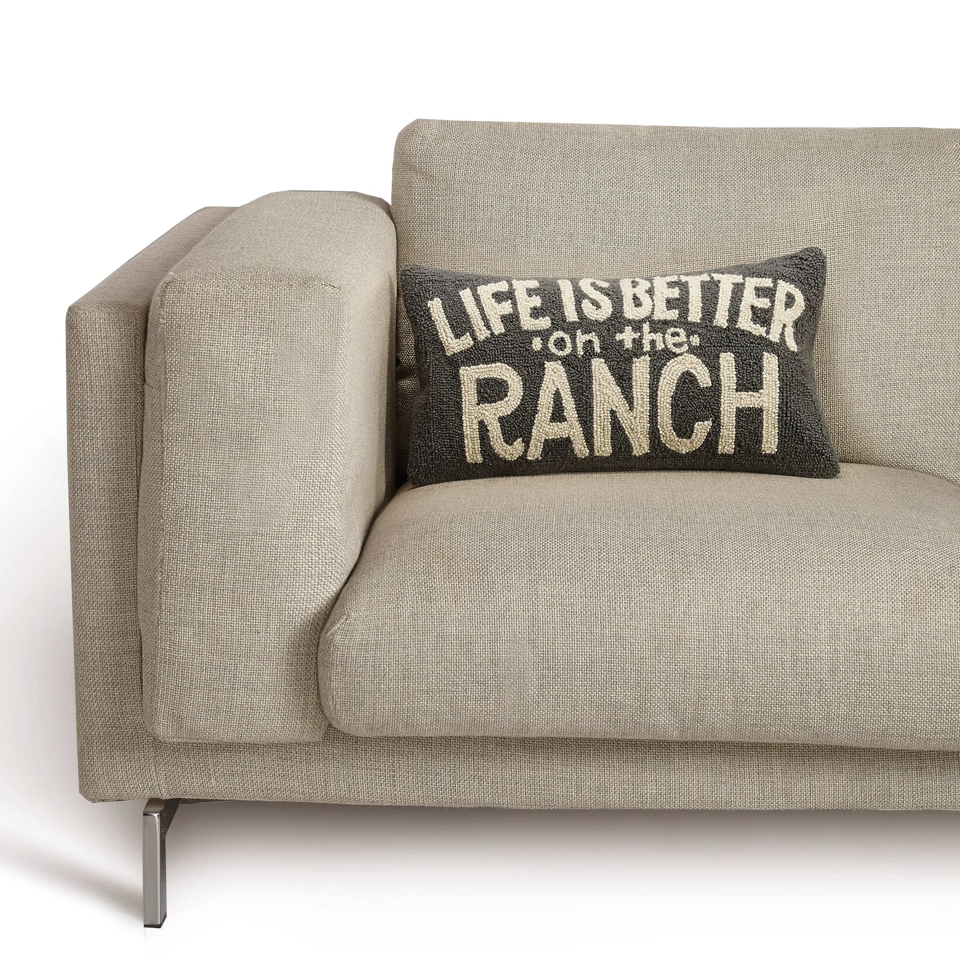 Beige sofa with a decorative pillow that reads 'Life is better on the ranch' on a white background