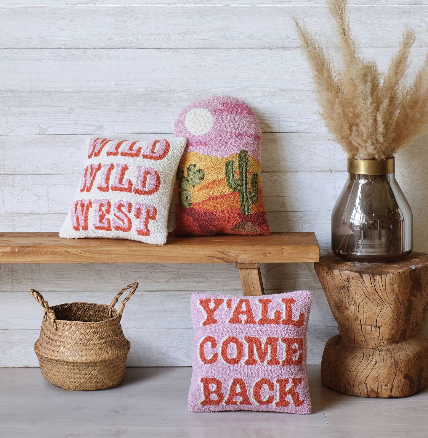 Decorative pillows with text and a cactus design on a wooden shelf against a white wall.
