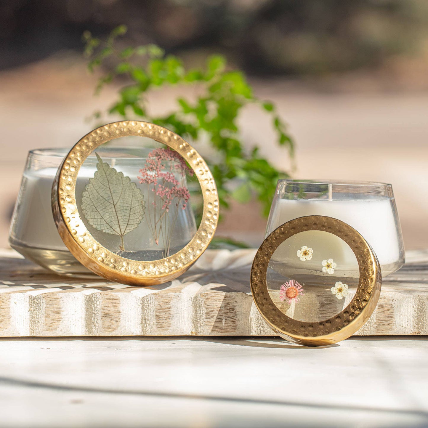 Two gold circular frames with dried flowers on a wooden surface with candles in the background.