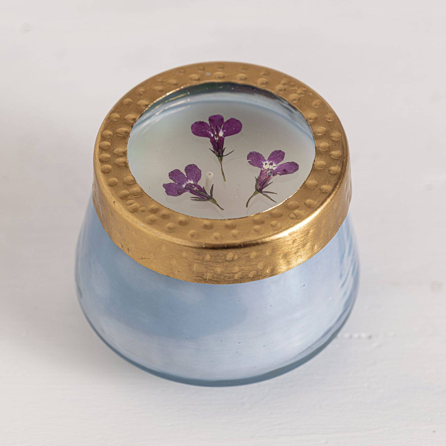 Glass jar with a gold lid featuring pressed purple flowers on a white background