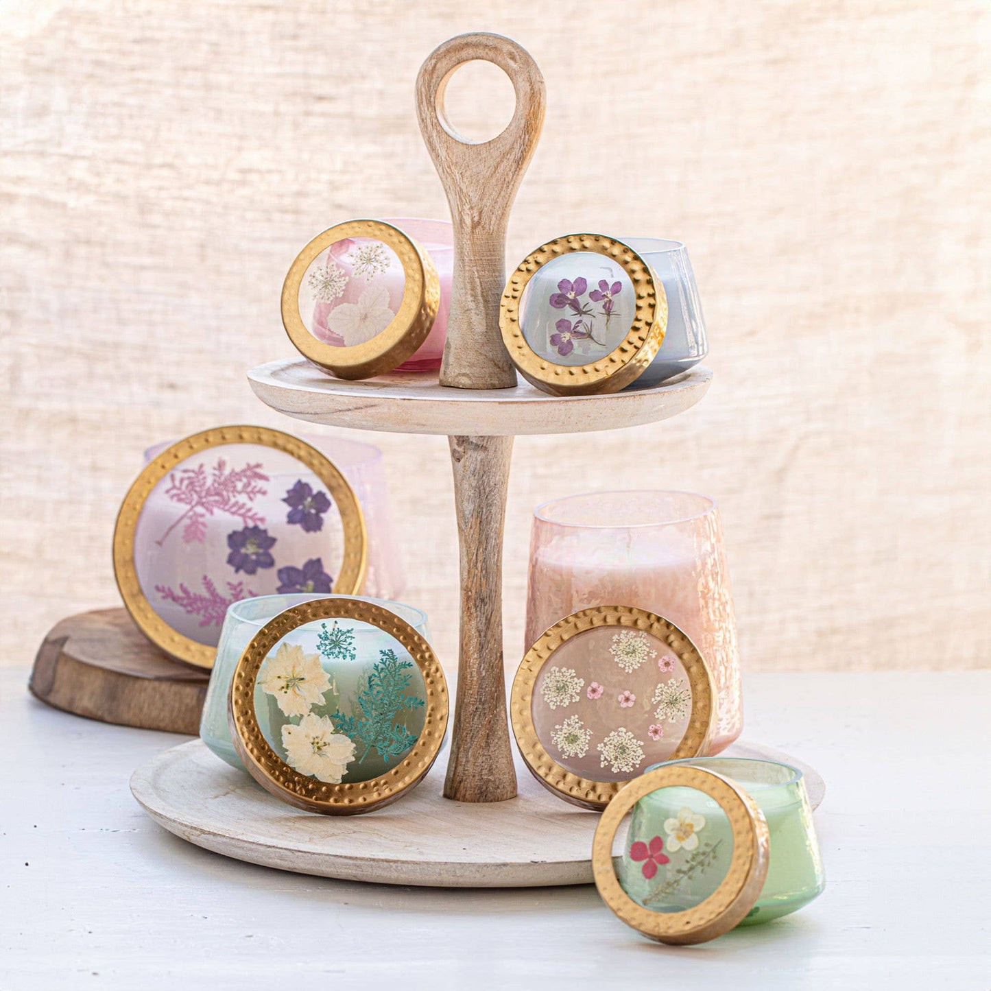 Decorative candles with floral designs on lids displayed on a wooden tiered stand.