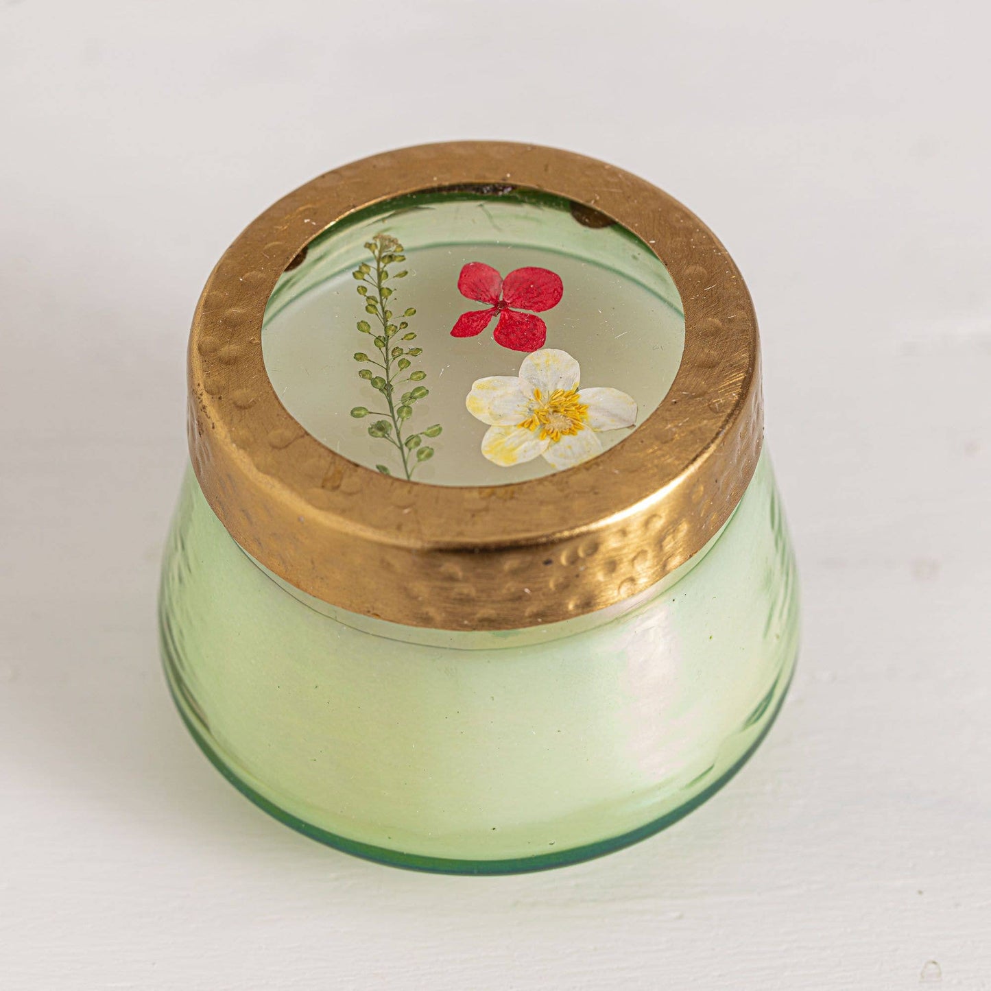 Green glass jar with a gold lid featuring pressed flowers on a white background