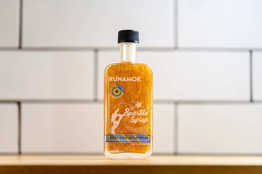 Bottle of Runamok Sparkle Syrup on a white tiled wall background