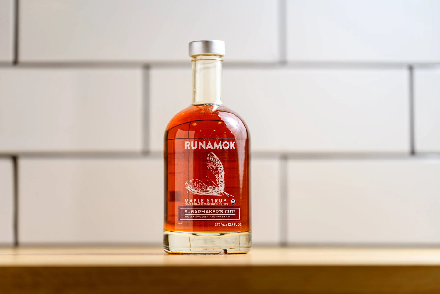 Bottle of Runamok maple syrup on a wooden surface with a tiled wall background