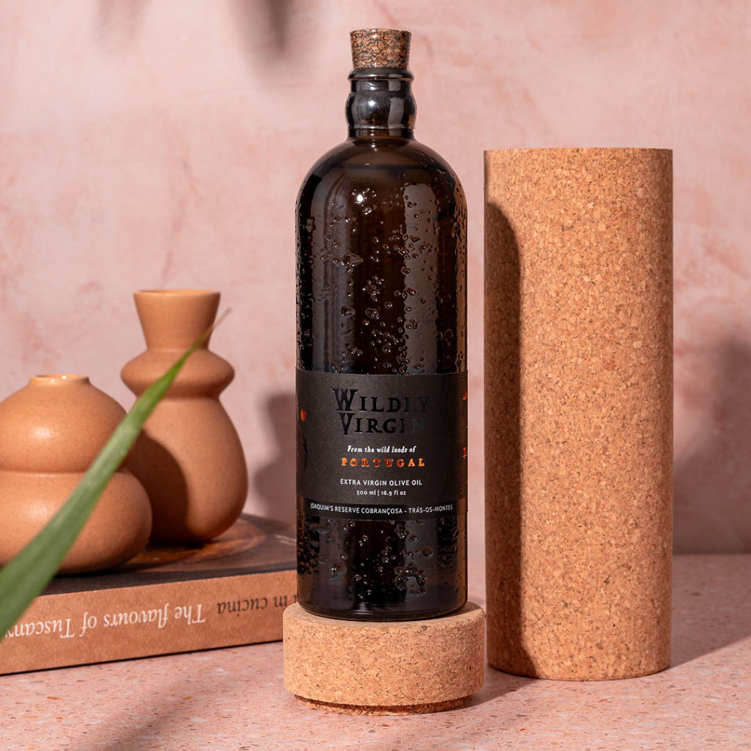 Bottle of Wildly Virgin olive oil on a cork stand with decorative vases in the background.