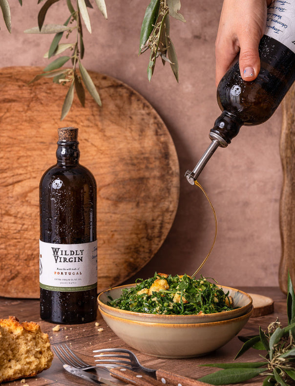 Bottle of Wildly Virgin olive oil being drizzled over a salad with a rustic background.