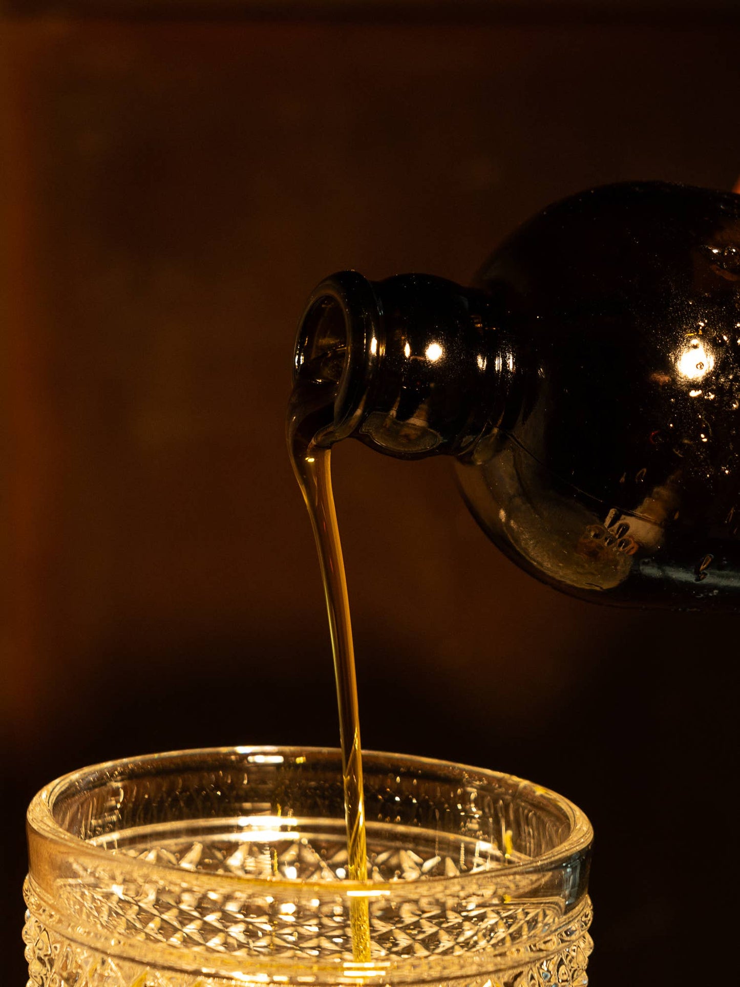 Liquid being poured from a bottle into a glass against a dark background